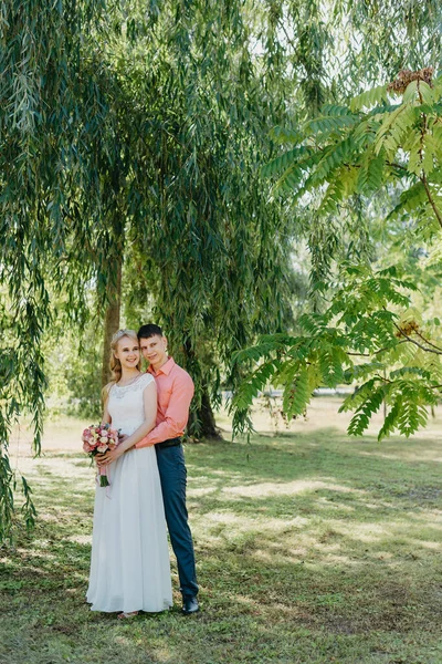 Novia y novio en el día de la boda caminando al aire libre en la naturaleza de primavera. Pareja nupcial, feliz mujer recién casada y hombre abrazándose en el parque verde. Amar pareja de boda al aire libre. Boda de novia y novio en —  Fotos de Stock