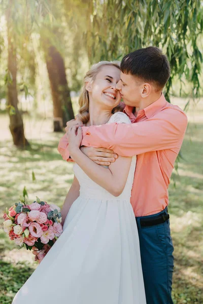 Noiva e noivo no dia do casamento andando ao ar livre na natureza de primavera. Casal nupcial, mulher recém-casada feliz e homem abraçando no parque verde. Casal de amor ao ar livre. Tiro de casamento de noiva e noivo em — Fotografia de Stock