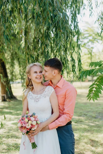 Noiva e noivo no dia do casamento andando ao ar livre na natureza de primavera. Casal nupcial, mulher recém-casada feliz e homem abraçando no parque verde. Casal de amor ao ar livre. Tiro de casamento de noiva e noivo em — Fotografia de Stock