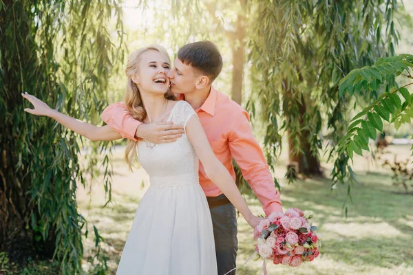 Noiva e noivo no dia do casamento andando ao ar livre na natureza de primavera. Casal nupcial, mulher recém-casada feliz e homem abraçando no parque verde. Casal de amor ao ar livre. Tiro de casamento de noiva e noivo em — Fotografia de Stock