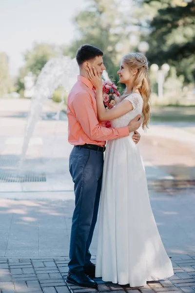 噴水の近くの結婚式の歩く上で幸せな花嫁と新郎。花嫁と新郎は結婚式の日にロマンチックな瞬間を持っています. — ストック写真