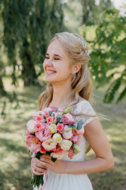 Açık havada çiçekli gelin. Orman parkında bir buket çiçekle uzun beyaz gelinlik içinde güzel bir gelinin portresi. Moda gelinliği içinde, doğal bir geçmişi olan güzel bir gelin.