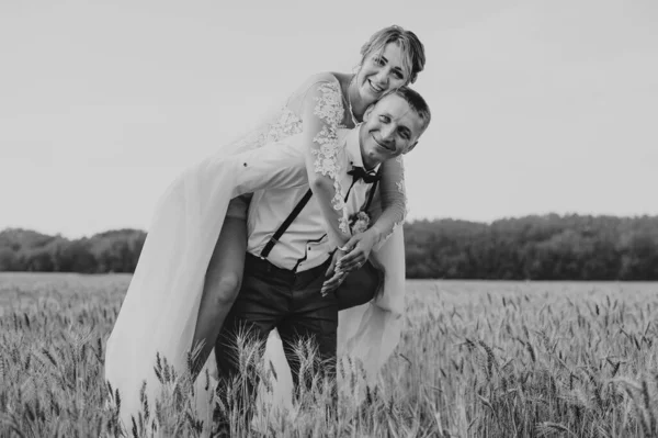 在阳光灿烂的日子，一对时尚而快乐的新人在麦田里举行婚礼。新娘和新郎在麦田里接吻.年轻漂亮的新婚夫妇拥抱在草地上. — 图库照片