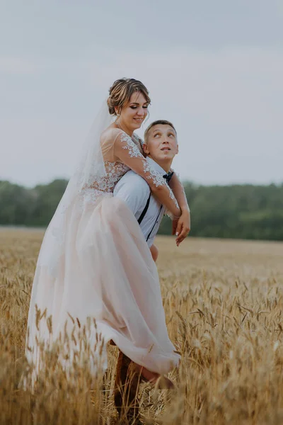 Casal de casamento elegante e feliz no campo de trigo no dia ensolarado. Noiva e noivo beijando em um campo de trigo. Jovem lindo casamento casal abraçando em um campo com grama encravada. — Fotografia de Stock