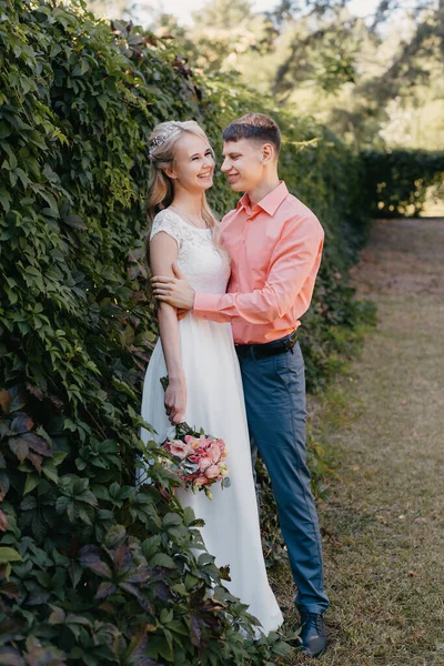 Noiva e noivo no dia do casamento andando ao ar livre na natureza de primavera. Casal nupcial, mulher recém-casada feliz e homem abraçando no parque verde. Casal de amor ao ar livre. Tiro de casamento de noiva e noivo em — Fotografia de Stock