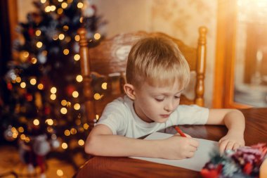 Noel Çocuğu Noel Baba 'ya mektup yaz, Dilek Listesi Yazan Çocuk, Odaklanmamış Işıklar Arkaplanı. 6 yaşında bir çocuk Noel Baba 'ya mektup yazıyor.