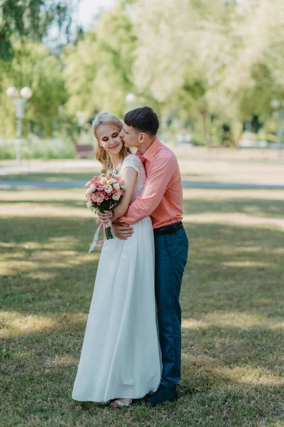 Noiva e noivo no dia do casamento andando ao ar livre na natureza de primavera. Casal nupcial, mulher recém-casada feliz e homem abraçando no parque verde. Casal de amor ao ar livre. Tiro de casamento de noiva e noivo em — Fotografia de Stock