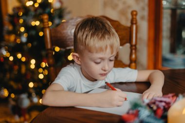 Noel Çocuğu Noel Baba 'ya mektup yaz, Dilek Listesi Yazan Çocuk, Odaklanmamış Işıklar Arkaplanı. 6 yaşında bir çocuk Noel Baba 'ya mektup yazıyor.