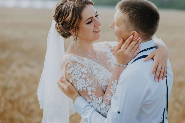 Fashionabla och glada bröllop par på vetefält på solig dag. Brud och brudgum kyssas på ett vetefält. Unga vackra bröllop par kramas i ett fält med gräs örat. — Stockfoto
