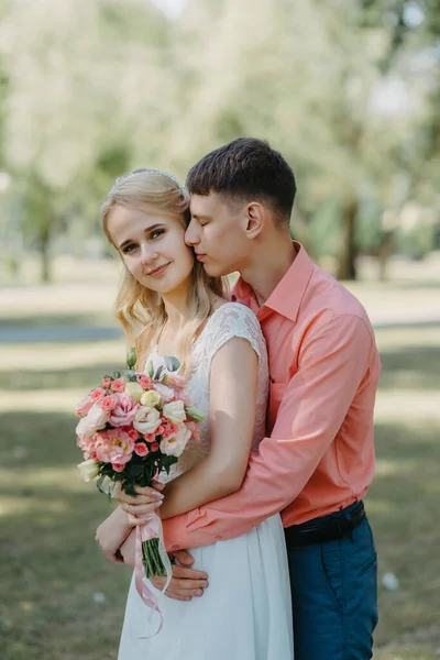 Novia y novio en el día de la boda caminando al aire libre en la naturaleza de primavera. Pareja nupcial, feliz mujer recién casada y hombre abrazándose en el parque verde. Amar pareja de boda al aire libre. Boda de novia y novio en — Foto de Stock