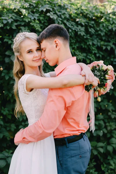 Noiva e noivo no dia do casamento andando ao ar livre na natureza de primavera. Casal nupcial, mulher recém-casada feliz e homem abraçando no parque verde. Casal de amor ao ar livre. Tiro de casamento de noiva e noivo em — Fotografia de Stock