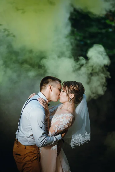 Bride and groom with the blue and yellow colored smoke bombs in the summer park. The bride and groom with the colored smoke at the background of summer forest. Wedding couple runs color smoke in the — Stock Photo, Image