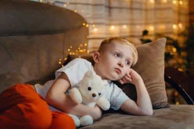 Kafkasyalı çocuk oyuncak ayıyla kanepede yatıyor. Sevimli küçük çocuk oyuncak ayıya sarılıyor ve evdeki kanepede yatıyor..