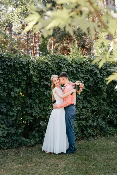 Noiva e noivo no dia do casamento andando ao ar livre na natureza de primavera. Casal nupcial, mulher recém-casada feliz e homem abraçando no parque verde. Casal de amor ao ar livre. Tiro de casamento de noiva e noivo em — Fotografia de Stock