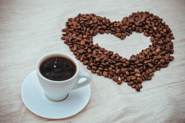 Kaffeetasse vorhanden. Kaffeebohnen in Herzform. Kaffeebohnen isoliert auf weißem Hintergrund. geröstete Kaffeebohnen, können als Hintergrund verwendet werden. — Stockfoto