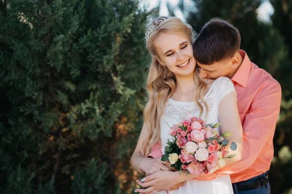 Novia y novio en el día de la boda caminando al aire libre en la naturaleza de primavera. Pareja nupcial, feliz mujer recién casada y hombre abrazándose en el parque verde. Amar pareja de boda al aire libre. Boda de novia y novio en — Foto de Stock