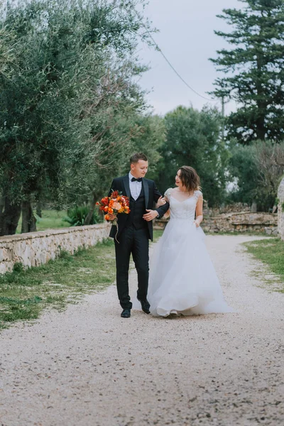 Feliz casal sorridente elegante andando na Toscana, Itália, no dia do seu casamento. A noiva e o noivo caminham pela rua pelas mãos. Um jovem e elegante casal caminha. Marido e esposa se comunicam bem — Fotografia de Stock