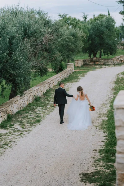 Счастливая стильная улыбающаяся пара, гуляющая в Тоскане, Италия, в день своей свадьбы. Жених и невеста идут по улице руками. Стильная молодая пара гуляет. Муж и жена хорошо общаются. — стоковое фото