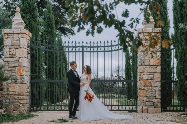 Feliz casal sorridente elegante andando na Toscana, Itália, no dia do seu casamento. A noiva e o noivo caminham pela rua pelas mãos. Um jovem e elegante casal caminha. Marido e esposa se comunicam bem — Fotografia de Stock