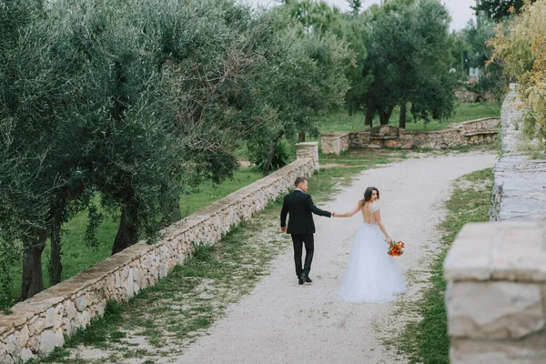 Happy stylish smiling couple walking in Tuscany, Italy on their wedding day. The bride and groom walk down the street by the hands. A stylish young couple walks. Husband and wife communicate nicely — Stock Photo, Image