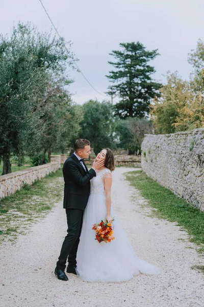 Feliz casal sorridente elegante andando na Toscana, Itália, no dia do seu casamento. A noiva e o noivo caminham pela rua pelas mãos. Um jovem e elegante casal caminha. Marido e esposa se comunicam bem — Fotografia de Stock