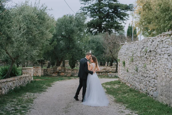 Felice elegante coppia sorridente passeggiando in Toscana, Italia il giorno del loro matrimonio. Gli sposi camminano per strada per le mani. Una giovane coppia elegante cammina. Marito e moglie comunicano bene — Foto Stock