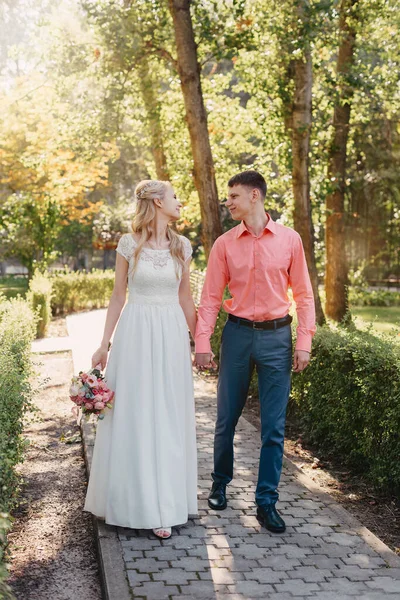 Noiva e noivo no dia do casamento andando ao ar livre na natureza de primavera. Casal nupcial, mulher recém-casada feliz e homem abraçando no parque verde. Casal de amor ao ar livre. Tiro de casamento de noiva e noivo em — Fotografia de Stock