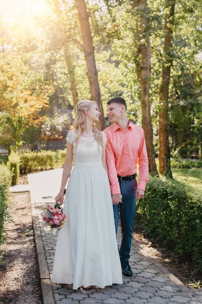 Noiva e noivo no dia do casamento andando ao ar livre na natureza de primavera. Casal nupcial, mulher recém-casada feliz e homem abraçando no parque verde. Casal de amor ao ar livre. Tiro de casamento de noiva e noivo em — Fotografia de Stock