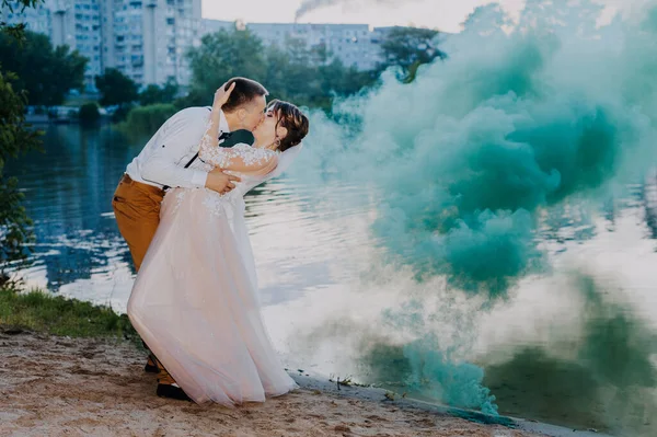 Noiva e noivo com as bombas de fumaça coloridas azuis e amarelas no parque de verão. A noiva e o noivo com a fumaça colorida no fundo da floresta de verão. Casamento casal corre fumaça cor no — Fotografia de Stock