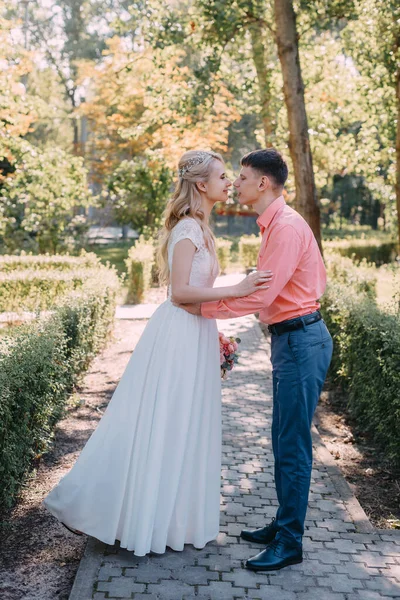 Noiva e noivo no dia do casamento andando ao ar livre na natureza de primavera. Casal nupcial, mulher recém-casada feliz e homem abraçando no parque verde. Casal de amor ao ar livre. Tiro de casamento de noiva e noivo em — Fotografia de Stock