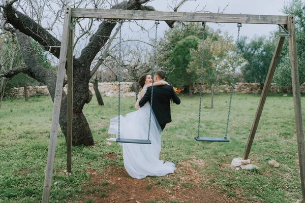 Feliz casal sorridente elegante andando na Toscana, Itália, no dia do seu casamento. Noviços com a troca no parque de estacionamento. A noiva e o noivo caminham pela rua pelas mãos. Um elegante jovem casal caminha — Fotografia de Stock