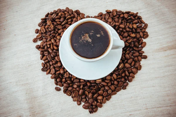 Ένα φλιτζάνι καφέ. Κόκκοι καφέ σε σχήμα καρδιάς. κόκκοι καφέ απομονωμένοι σε λευκό φόντο. ψημένα φασόλια καφέ, μπορεί να χρησιμοποιηθεί ως φόντο. — Φωτογραφία Αρχείου