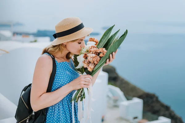 Hermosa chica caminando con ramo de flores a lo largo de la calle de la isla de Santorini, una antigua ciudad europea, Grecia. Retrato de una chica turística caminando sobre el fondo de la calle. Historia de amor verano — Foto de Stock