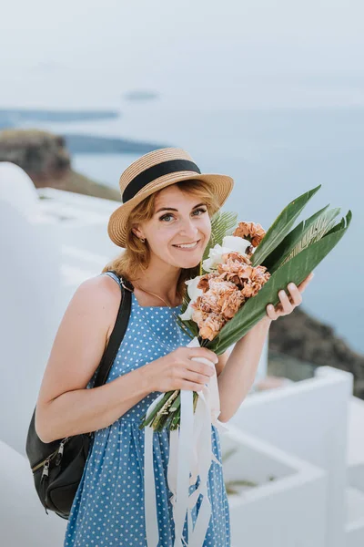 Mooi meisje wandelen met boeket bloemen langs de straat van Santorini eiland, een oude Europese stad, Griekenland. Portret van een toeristisch meisje op straat. Liefdesverhaal zomer — Stockfoto