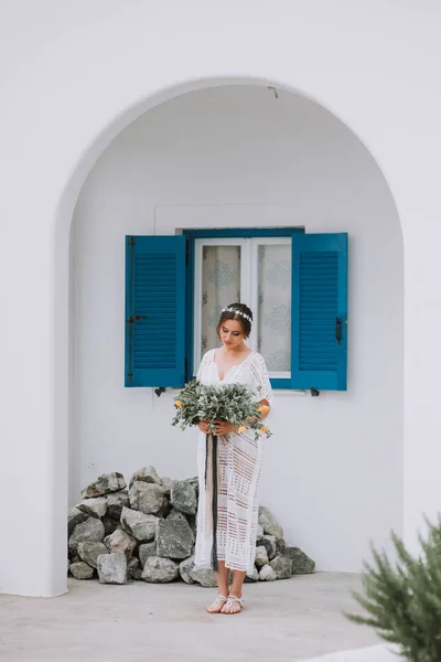 Hermosa novia en un fondo de arquitectura blanca con ventana azul en la isla de Santorini, Grecia, un destino de boda popular — Foto de Stock