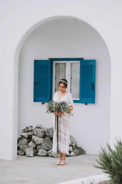 Guapo hermosa novia caucásica posando cerca de la pared blanca con ventanas azules. Joven novia atractiva con el ramo de flores — Foto de Stock