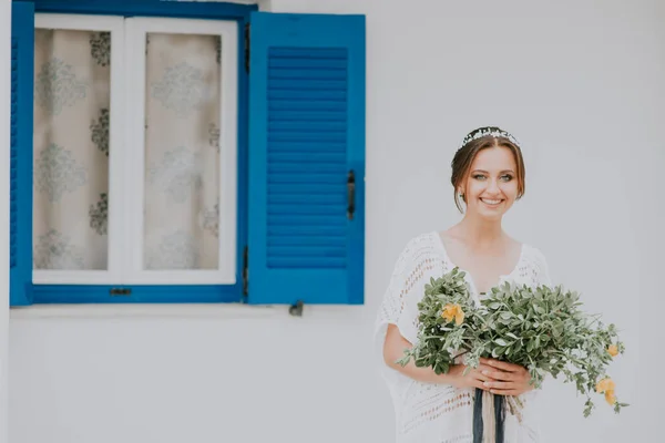 Handsome beautiful caucasian bride posing near white wall with blue windows. Young attractive bride with the bouquet of flowers — Stock Photo, Image