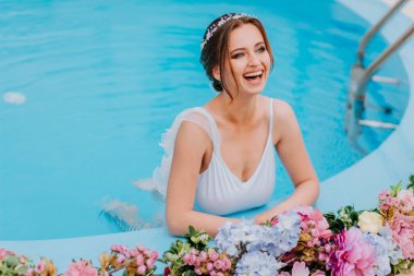 Güzel beyaz mayo ve çiçek çelenkleri içinde güzel bir gelin, turkuaz suda çiçekle yüzme havuzunda duruyor, güneşli bir günde su havuzunda güzel bir kız.