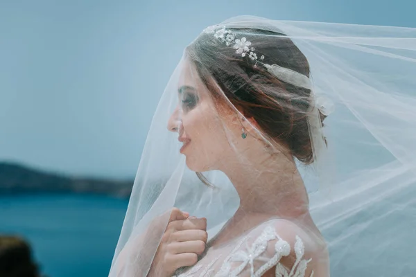 Romantická krásná nevěsta v bílých šatech pózuje na terase s mořem a horami v pozadí. — Stock fotografie