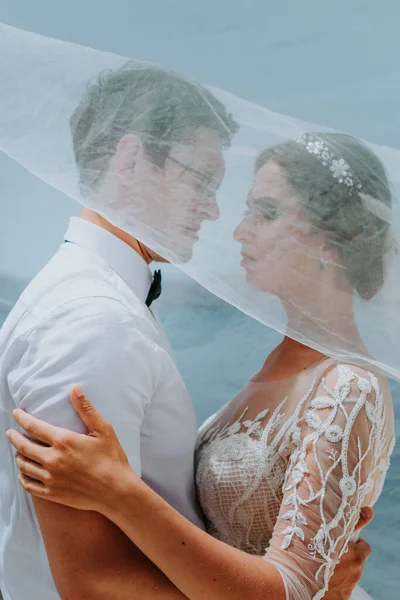 Schöne Braut und Bräutigam umarmen und küssen sich unter dem Brautschleier an ihrem Sommerhochzeitstag auf der griechischen Insel Santorin — Stockfoto