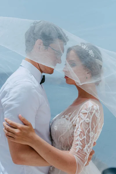 Gyönyörű menyasszony és vőlegény ölelés és csók alatt a menyasszonyi fátyol a nyári esküvő napján a görög szigeten Santorini — Stock Fotó