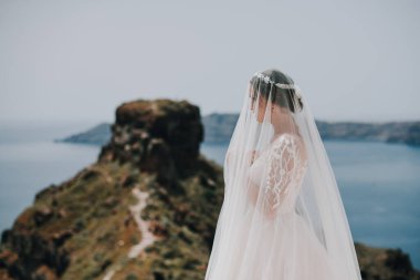 Beyaz elbiseli romantik gelin terasta poz veriyor. Arka planda dağlar ve deniz var.