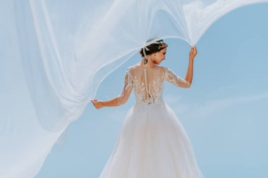 Beyaz elbiseli romantik gelin terasta poz veriyor. Arka planda dağlar ve deniz var.