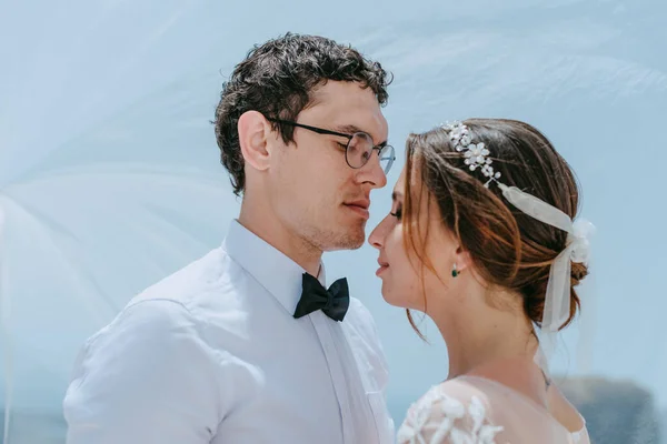 Hermosa novia y novio abrazos y besos bajo el velo nupcial en su día de la boda de verano en la isla griega Santorini — Foto de Stock