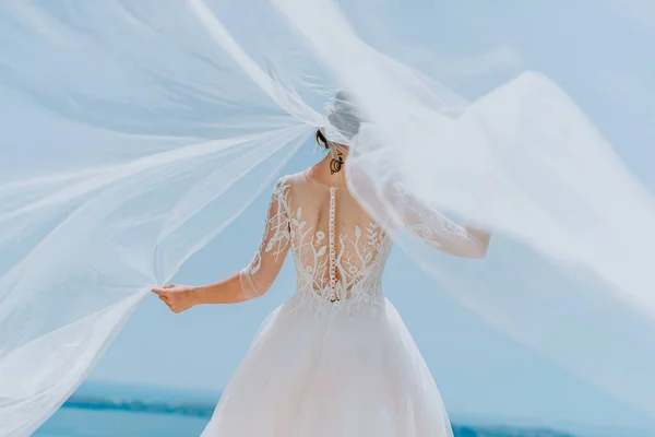 Романтическая красивая невеста в белом платье позирует на террасе с морем и горами на заднем плане — стоковое фото