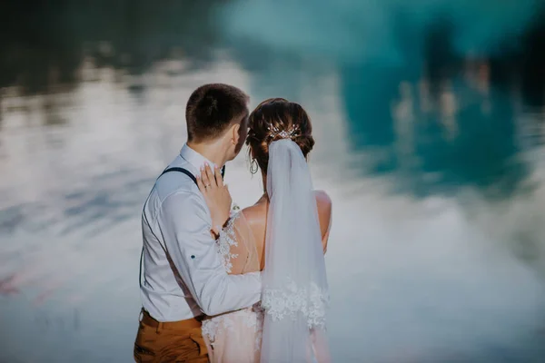 Bride and groom with the blue and yellow colored smoke bombs in the summer park. The bride and groom with the colored smoke at the background of summer forest. Wedding couple runs color smoke in the — Fotografia de Stock