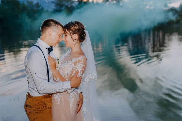 Bride and groom with the blue and yellow colored smoke bombs in the summer park. The bride and groom with the colored smoke at the background of summer forest. Wedding couple runs color smoke in the — Foto Stock