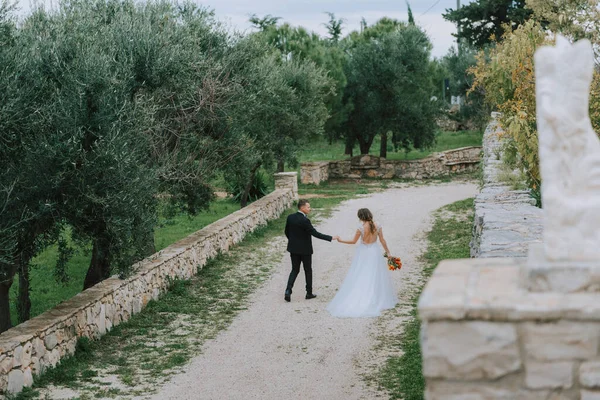 Felice elegante coppia sorridente passeggiando in Toscana, Italia il giorno del loro matrimonio. Gli sposi camminano per strada per le mani. Una giovane coppia elegante cammina. Marito e moglie comunicano bene — Foto Stock