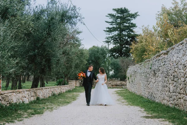 Felice elegante coppia sorridente passeggiando in Toscana, Italia il giorno del loro matrimonio. Gli sposi camminano per strada per le mani. Una giovane coppia elegante cammina. Marito e moglie comunicano bene — Foto Stock