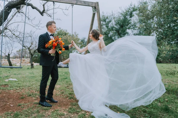 Felice elegante coppia sorridente passeggiando in Toscana, Italia il giorno del loro matrimonio. NEWLYWEDS con l'altalena nel parco. Gli sposi camminano per strada per le mani. Una giovane coppia alla moda cammina — Foto Stock